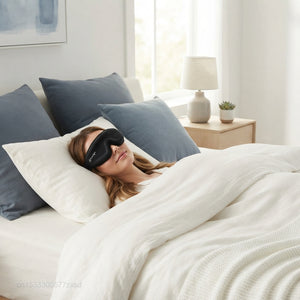 A person sleeping peacefully in a modern bedroom wearing a black 3D contoured sleep mask, surrounded by slate blue and white 